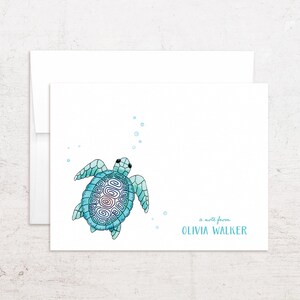 May include: White stationery card with a watercolor illustration of a blue sea turtle swimming upwards, with bubbles. The text "a note from OLIVIA WALKER" is printed in a matching blue color. A white envelope is behind the card.