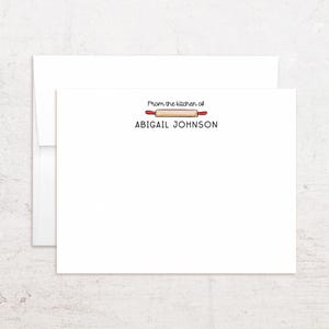 May include: White stationery set featuring a card and envelope. The card has the text "From the kitchen of" above a rolling pin illustration and the name "ABIGAIL JOHNSON" below. The rolling pin has red handles.