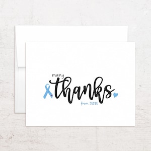 May include: A white folded greeting card with a matching envelope. The front features the black text "many thanks" in a script font, a light blue awareness ribbon with a small red heart, a light blue heart, and the blue text "from JESSE".