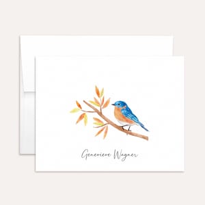May include: Watercolor illustration of a bluebird perched on a branch with autumn leaves. The bird has blue and orange plumage. The card includes the name "Genevieve Wagner" in script.