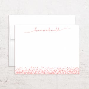 May include: A white stationery card and matching envelope featuring the name kara mcdonald in a pink cursive script at the top center and a border of small pink dots along the bottom edge of the card, creating a simple and clean design.