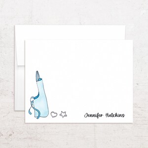 May include: White stationery set featuring a blue apron illustration, heart and star cookie cutters, and the name "Jennifer Hutchins" in black script. Includes a matching envelope. Ideal for personalized notes or gifts.