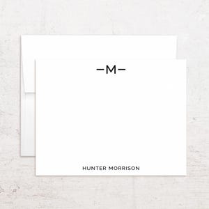 May include: White stationery set featuring a card and envelope. The card has a black letter "M" with horizontal lines above and below, and the name "HUNTER MORRISON" printed below the letter in black. The envelope is white.