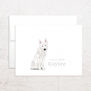 May include: White stationery card with a seated illustration of a white German Shepherd dog. The text "A NOTE FROM Kaylee" is printed in gray below the dog. A white envelope is behind the card.