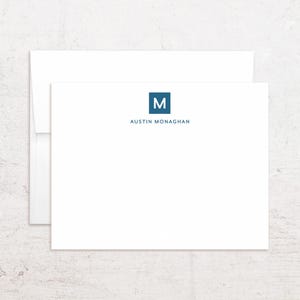 May include: White stationery set with a matching envelope. The stationery features a blue square with the letter "M" and the name "Austin Monaghan" printed below in a matching blue font. The stationery is clean and minimalist.