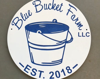 May include: White round sign with blue lettering that reads "Blue Bucket Farm, LLC - EST. 2018" with a blue illustration of a bucket in the center.