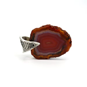 May include: A red agate pendant with a silver setting. The agate has a layered pattern of red, orange, and white. The silver setting has a textured design and a small black stone.
