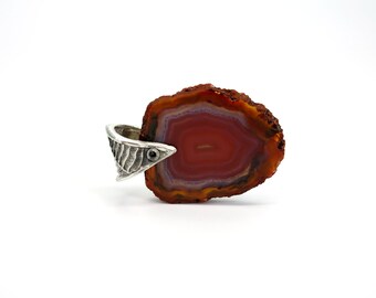 May include: A red agate pendant with a silver setting. The agate has a layered pattern of red, orange, and white. The silver setting has a textured design and a small black stone.
