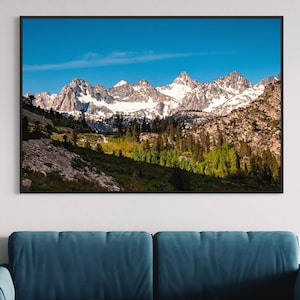 May include: A framed photograph of a mountain range with snow-capped peaks and a valley with green trees in the foreground. The sky is blue and there are clouds in the distance.