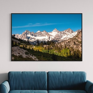 Puede incluir: Una fotograf&iacute;a enmarcada de una cordillera con picos cubiertos de nieve y un valle con &aacute;rboles verdes en primer plano. El cielo es azul y hay nubes en la distancia.