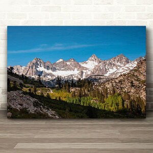 Puede incluir: Una vista panor&aacute;mica de una cordillera con picos cubiertos de nieve y un valle verde y exuberante en primer plano. El cielo es azul brillante con algunas nubes.