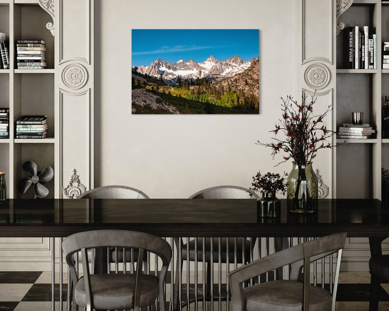 Puede incluir: Una fotograf&iacute;a panor&aacute;mica de una cordillera con picos cubiertos de nieve y un valle verde exuberante en primer plano. El cielo es azul brillante con algunas nubes.