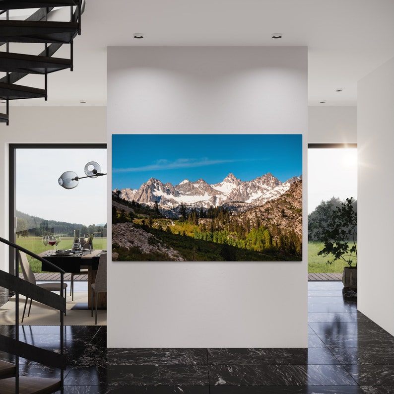 Puede incluir: Una fotograf&iacute;a panor&aacute;mica de una cordillera con picos cubiertos de nieve, &aacute;rboles verdes y un cielo azul. Las monta&ntilde;as est&aacute;n en el fondo y los &aacute;rboles en primer plano. El cielo es de un azul brillante y hay algunas nubes en el cielo.