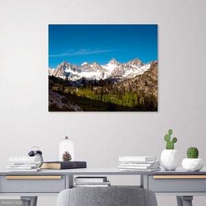 Puede incluir: Una fotograf&iacute;a panor&aacute;mica de una cordillera con picos cubiertos de nieve y un valle verde exuberante en primer plano. El cielo es azul brillante con algunas nubes.