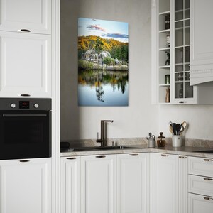 May include: A rectangular landscape canvas print depicting a serene lake scene with a rocky shoreline, lush green trees, and a colorful sunset. The artwork is displayed in a modern white kitchen setting.