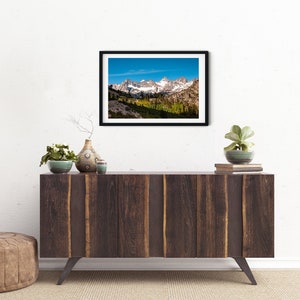 Puede incluir: Una fotograf&iacute;a enmarcada de una cordillera con picos cubiertos de nieve y un valle con &aacute;rboles en primer plano. El cielo es azul y hay nubes en la distancia.
