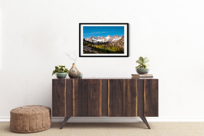 Puede incluir: Una fotograf&iacute;a enmarcada de una cordillera con picos cubiertos de nieve y un valle con &aacute;rboles en primer plano. El cielo es azul y hay nubes en la distancia.