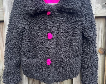 May include: A black, textured jacket with a large collar and three bright pink buttons. The jacket has a hot pink lining and the label "Gretchen Scott" is visible. The jacket is hanging on a black hanger.