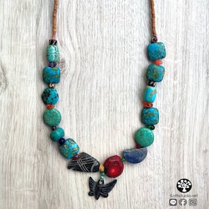 Peut inclure: Un collier de perles turquoise, rouge et noir avec un pendentif en forme de papillon. Le collier est fait de pierres naturelles et a un fermoir en or.
