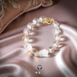 May include: A bracelet composed of clear, spherical crystal beads and two textured, irregular crystal beads. The beads are separated by small gold-toned metal spacers, and the piece is secured with a gold-toned clover-shaped toggle clasp.
