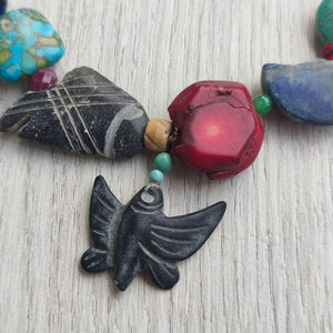 Peut inclure: Un collier de perles color&eacute;es avec un pendentif en forme de papillon en pierre noire sculpt&eacute;e. Le collier est compos&eacute; de perles turquoise, rouges, bleues et vertes.