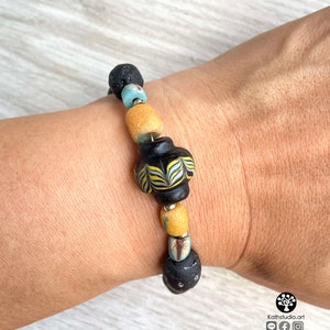 May include: A bracelet made with black lava rock beads, yellow and blue glass beads, and a black and white patterned glass bead.