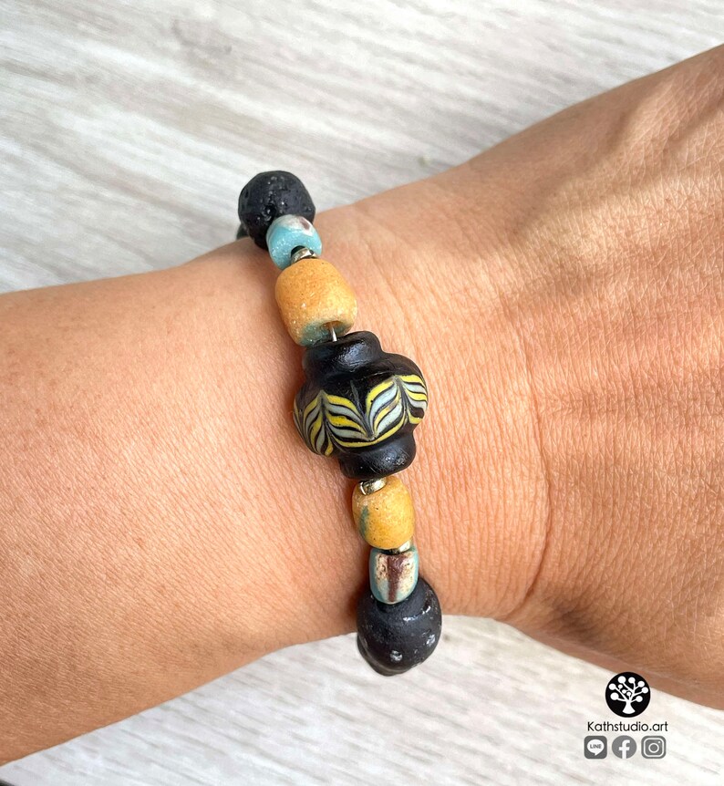 May include: A bracelet made with black lava rock beads, yellow and blue glass beads, and a black and white patterned glass bead.