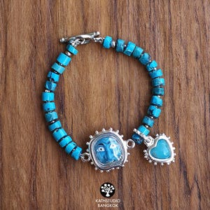 Puede incluir: Una pulsera con cuentas cil&iacute;ndricas de turquesa ensartadas en una cadena de plata con cierre de barra. La pieza incluye un dije central enmarcado en plata que representa un rostro azul y un colgante de turquesa en forma de coraz&oacute;n.