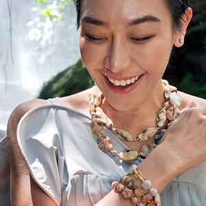 Puede incluir: Un conjunto de collar y pulsera de varias hebras con cuentas de piedra natural pulidas de forma irregular en tonos beige, bronce, marr&oacute;n y gris, acentuadas con peque&ntilde;os espaciadores de metal dorado y un cierre de barra dorado.