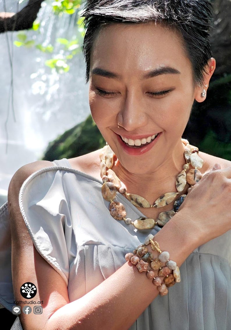 Puede incluir: Un conjunto de collar y pulsera de varias hebras con cuentas de piedra natural pulidas de forma irregular en tonos beige, bronce, marr&oacute;n y gris, acentuadas con peque&ntilde;os espaciadores de metal dorado y un cierre de barra dorado.