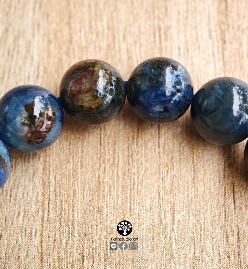 Pu&ograve; includere: Un bracciale composto da perline sferiche lucide in tonalit&agrave; blu intenso, caratterizzate da inclusioni naturali marrone scuro e nere all'interno della struttura della pietra. Le perline sono infilate su un cordino blu, con il testo Kathstudio.art visibile.