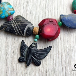 Peut inclure: Un collier color&eacute; avec diff&eacute;rentes pierres et un pendentif en forme d'oiseau noir sculpt&eacute;. Le collier comprend des pierres turquoise, rouges, bleues et vertes.