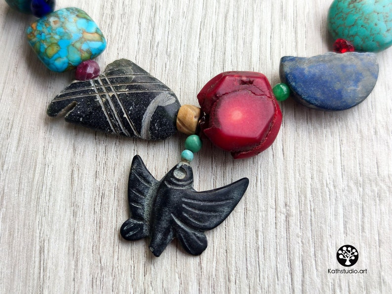 Peut inclure: Un collier color&eacute; avec diff&eacute;rentes pierres et un pendentif en forme d'oiseau noir sculpt&eacute;. Le collier comprend des pierres turquoise, rouges, bleues et vertes.