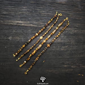 May include: Four beaded bracelets featuring brown and gold tiger eye stones, interspersed with metallic gold-toned spacers and cylindrical beads. Each bracelet is finished with a gold-toned lobster clasp. The text Kathstudio.art is visible.