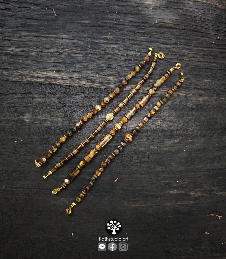 May include: Four beaded bracelets featuring brown and gold tiger eye stones, interspersed with metallic gold-toned spacers and cylindrical beads. Each bracelet is finished with a gold-toned lobster clasp. The text Kathstudio.art is visible.