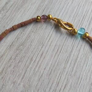 Peut inclure: Un collier de perles brun et or avec un fermoir en or et des perles de verre roses et bleues.