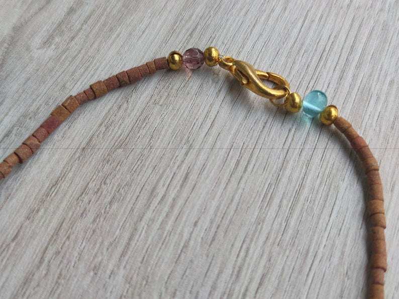 Peut inclure: Un collier de perles brun et or avec un fermoir en or et des perles de verre roses et bleues.