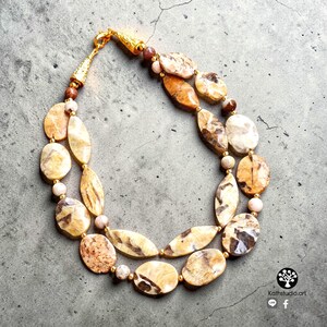 Puede incluir: Un collar de dos hilos con piedras pulidas de forma ovalada con patrones en beige y marr&oacute;n, intercaladas con peque&ntilde;as cuentas redondas de colores claros. El collar cuenta con herrajes de metal dorado y un cierre de tono dorado.