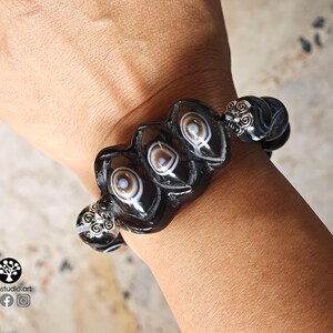 May include: A stretch bracelet featuring black and white banded agate beads with distinct eye-like patterns. The bracelet includes silver-toned metal spacers with intricate filigree scrollwork designs between the larger, oval-shaped agate beads.