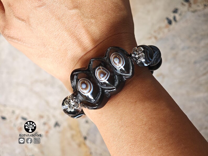 May include: A stretch bracelet featuring black and white banded agate beads with distinct eye-like patterns. The bracelet includes silver-toned metal spacers with intricate filigree scrollwork designs between the larger, oval-shaped agate beads.