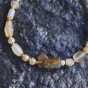 May include: A beaded bracelet featuring translucent, irregularly shaped light-colored stone beads interspersed with small, round, metallic gold-tone spacer beads. A central carved stone animal figure is positioned among the beads.