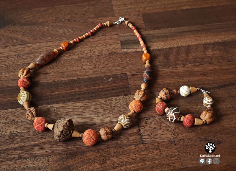 May include: A necklace and bracelet set featuring a variety of beads in shades of brown, orange, and cream. The necklace has a mix of round and oblong beads, with a large, textured stone-like bead. The bracelet mirrors the necklace's design.