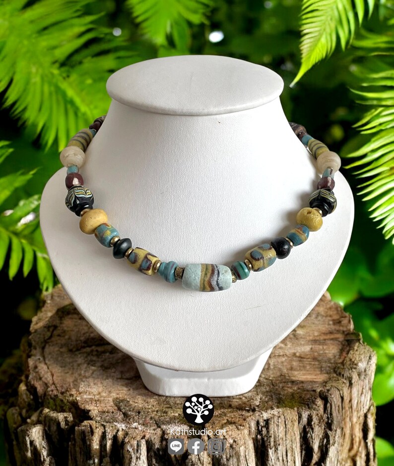 May include: A necklace made of colorful glass beads, including blue, yellow, and black beads. The necklace has a larger, striped, light blue bead in the center.