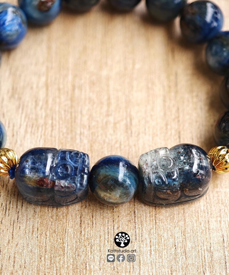 Pu&ograve; includere: Un braccialetto con perline di cianite blu lucide, due figure di animali intagliate in cianite e distanziatori in metallo dorato. Le perline mostrano tonalit&agrave; blu intenso con inclusioni naturali. Il testo Kathstudio.art &egrave; visibile in basso.