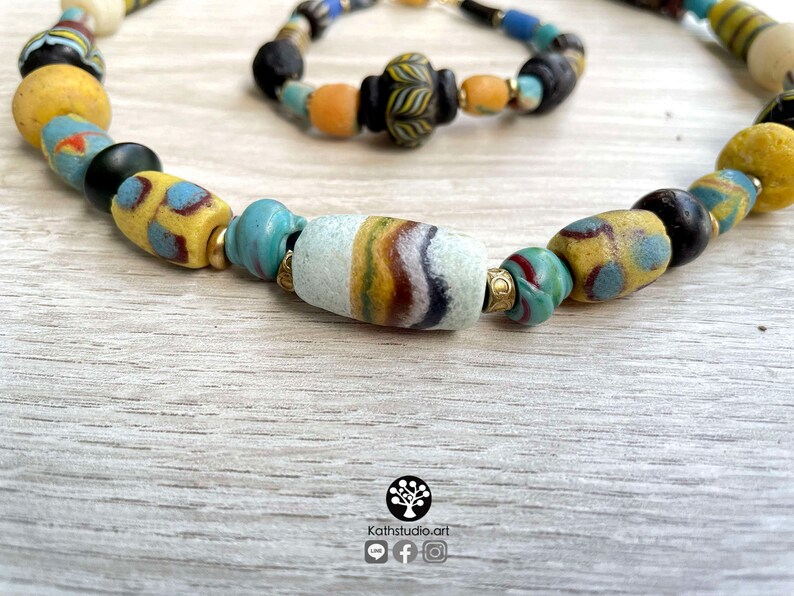 May include: A colorful beaded necklace with a variety of blue, yellow, and white glass beads. The necklace is made of vintage glass beads and has a unique, bohemian style.