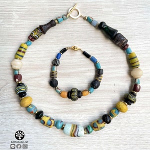 May include: A colorful necklace and bracelet made of vintage glass beads. The necklace features a variety of colors, including yellow, blue, green, and black. The bracelet is a similar style, with a smaller size and a gold clasp.