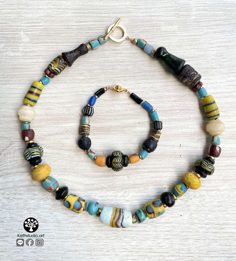 May include: A colorful necklace and bracelet made of vintage glass beads. The necklace features a variety of colors, including yellow, blue, green, and black. The bracelet is a similar style, with a smaller size and a gold clasp.