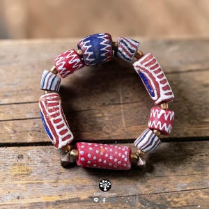 May include: A circular bracelet composed of cylindrical beads in red, blue, and white with various patterns including zigzags, stripes, and dots. Small metallic spacer beads are positioned between each larger patterned bead in the design.