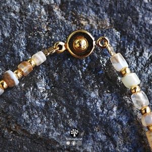May include: A beaded bracelet featuring alternating translucent, earth-toned stone beads and small gold-colored metallic spheres. The bracelet is secured with a circular gold-colored magnetic clasp. The text Kathstudio.art is visible at the bottom.
