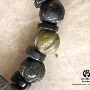 Puede incluir: Una pulsera de cuentas que alterna cuentas negras redondas y cuentas esf&eacute;ricas de color verde oliva talladas. Las cuentas negras est&aacute;n intercaladas con espaciadores negros finos y planos. La imagen incluye el texto KATHSTUDIO BANGKOK TURNING HERITAGE INTO EVERYDAY ELEGANCE.